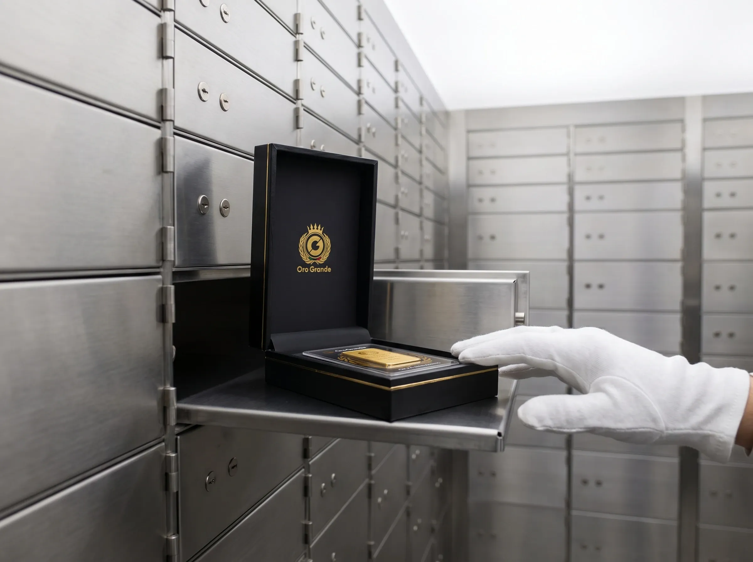 Una mano con il guanto bianco sul cassetto di una cassetta di sicurezza, con dentro il cofanetto di un lingotto
