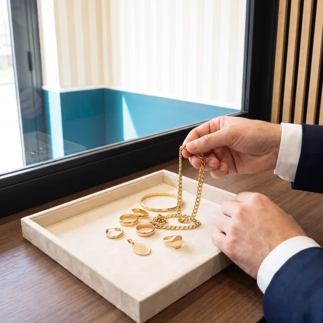 L’esperto solleva una catena d’oro dal vassoio, accanto a fedi, un bracciale, un orecchino spaiato, una medaglietta e un anello con sigillo