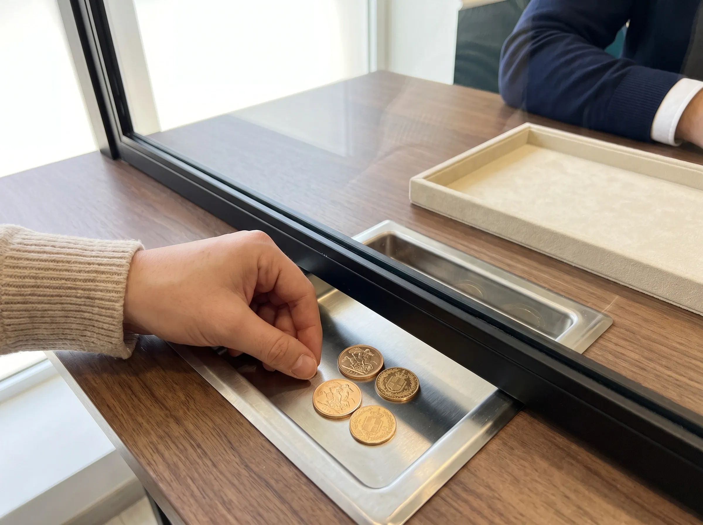 Una mano passa alcune monete d’oro nel passa-oggetti della cassa vetrata